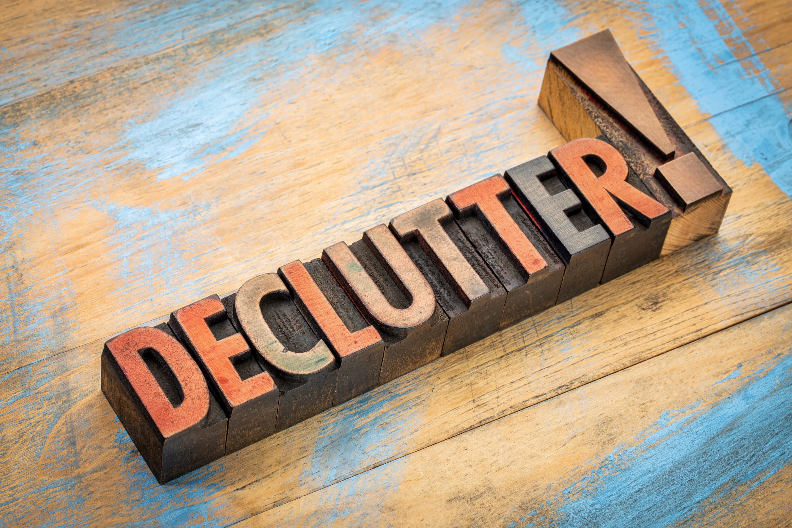 Wood block spelling out "Declutter!" on a wooden surface.